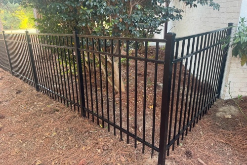 Black ornamental metal fence installed around a landscaped tree area beside a building in Fayetteville, NC