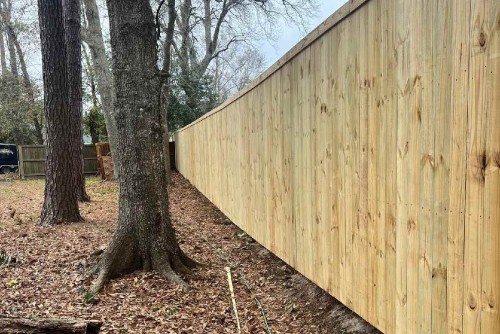 Wood privacy fence installation in Fayetteville, NC along wooded backyard with natural pine panels and sloped design